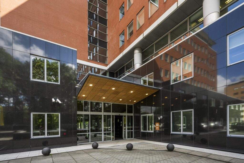 Ingang van een modern kantoorgebouw aan het Koningin Wilhelminaplein met zwarte gevelpanelen en grote ramen.